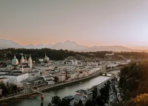 Aerial view of Salzburg showing river, bridges, historic buildings, and mountains in the background at sunset.